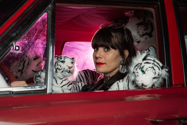 Portrait of solo artist Glockabelle sitting in the driver seat of a car filled with tiger stuffed animals.