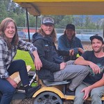 Four members of BITTER//WASHED are seated in a yellow golf cart.