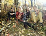 Photo taken in a forest setting in autumn, of fourpiece Cheer. Each member is sitting in the grass.