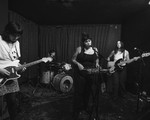 Black and white photo of four-piece Eraser performing on stage with a guitar, bass, keyboard and drums