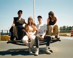 A colour photo of four-piece Stem Champ sitting on a picnic table in an empty outdoor parking lot with a clear blue sky behind them