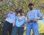 A colour photo shows three-piece band Tawni Bias posing in front of a leafy tree on a sunny day