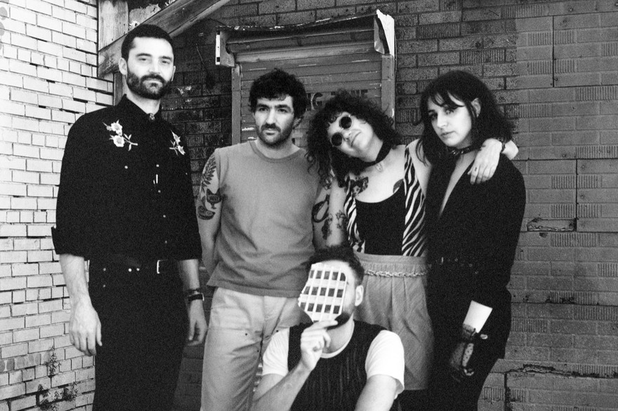 A black and white photo shows five-piece band Uncanny Valley posing in a back alley.